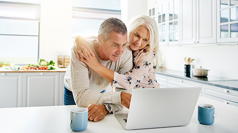 Older couple looking at their computer together in a bright kitchen.
